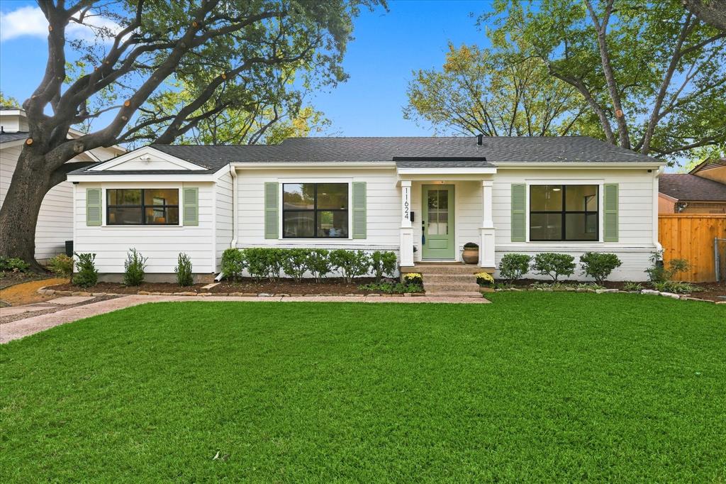 Single-story exterior featuring white horizontal siding, sage green shutters, a covered front entryway with square columns, and a mature shade tree Single-story exterior featuring white horizontal siding, sage green shutters, a covered front entryway with square columns, and a mature shade tree