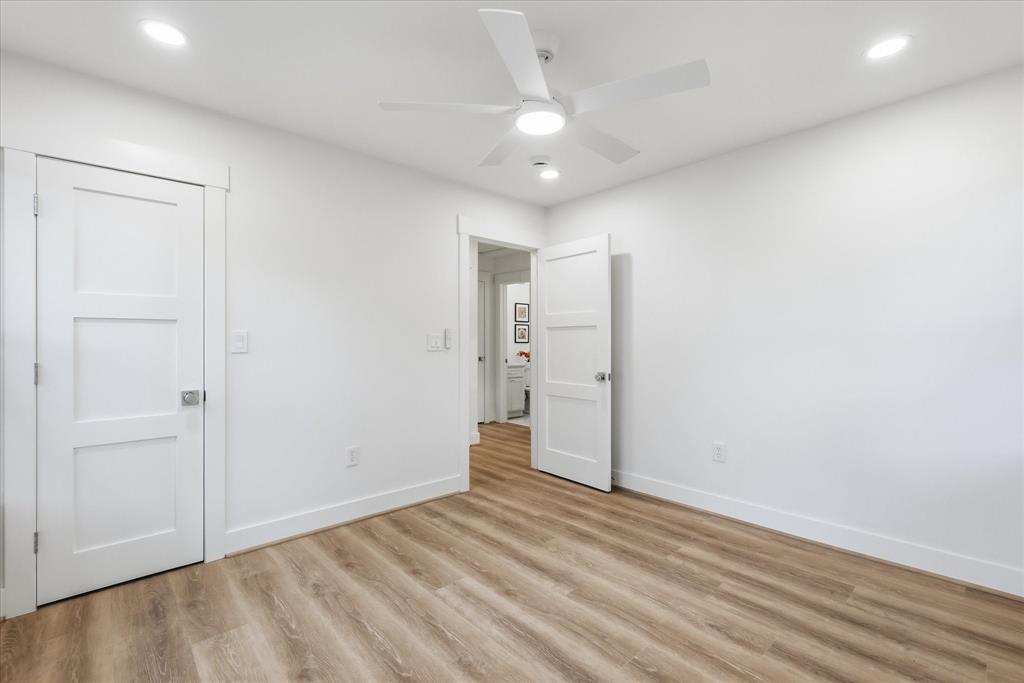 Wood-finish flooring, white three-panel interior doors, recessed lighting, and a modern white ceiling fan with integrated light