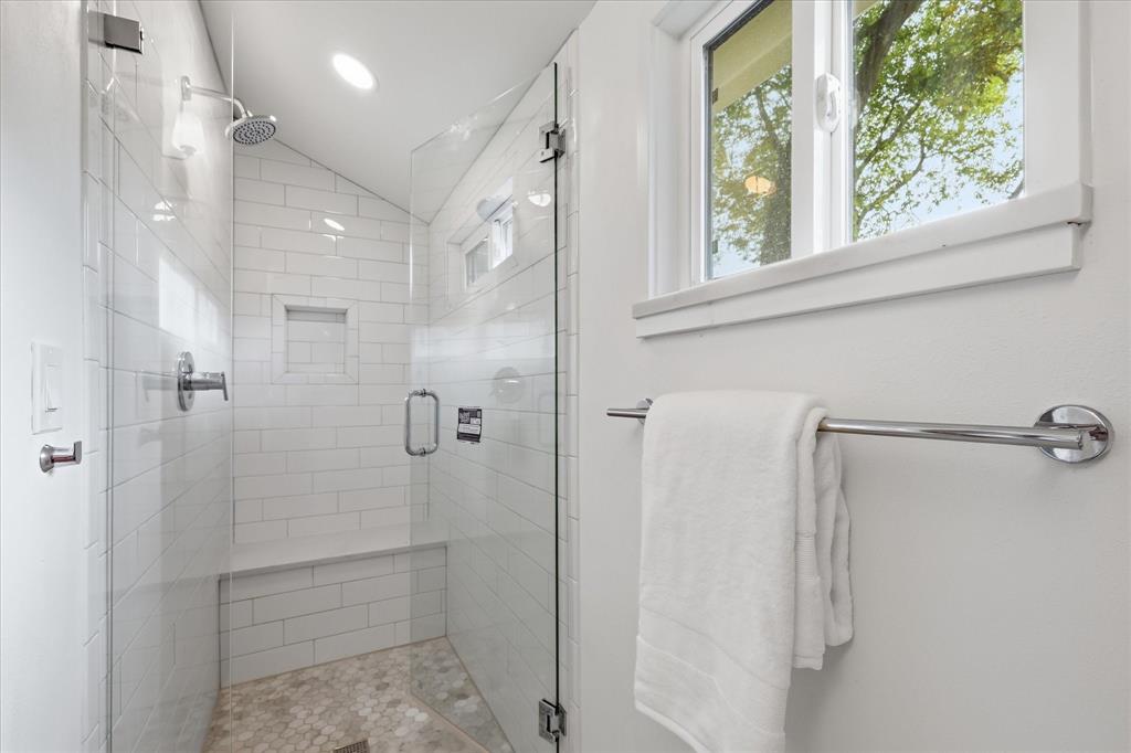Walk-in shower featuring subway tile surround, built-in bench, glass enclosure, recessed wall niche, and natural stone pebble flooring