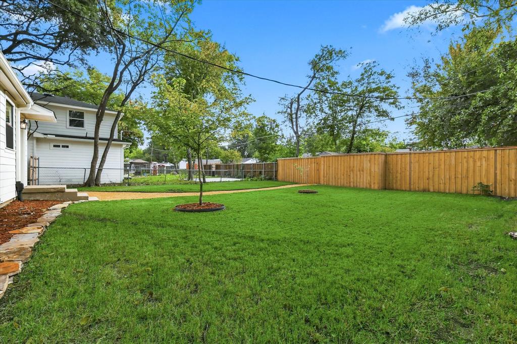 Backyard featuring a wood privacy fence, stone landscape edging, grass lawn, and gravel pathway