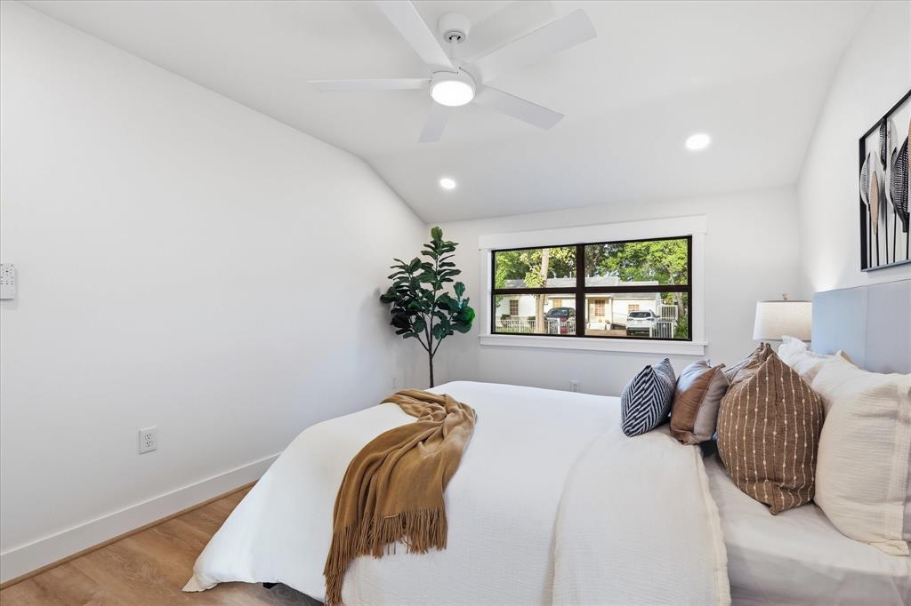Vaulted ceiling with white ceiling fan, recessed lighting, wood-finish flooring, and large window with dark-frame trim