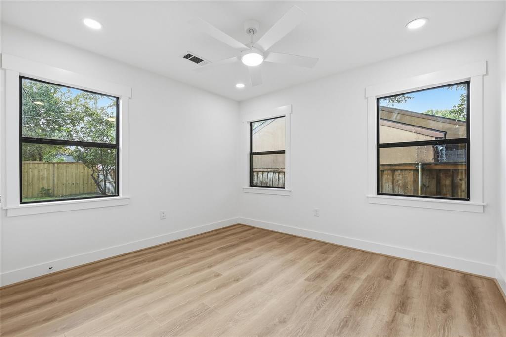 Interior room featuring wood-finish flooring, white walls, three windows with black frames and white trim, recessed lighting, and a white ceiling fan