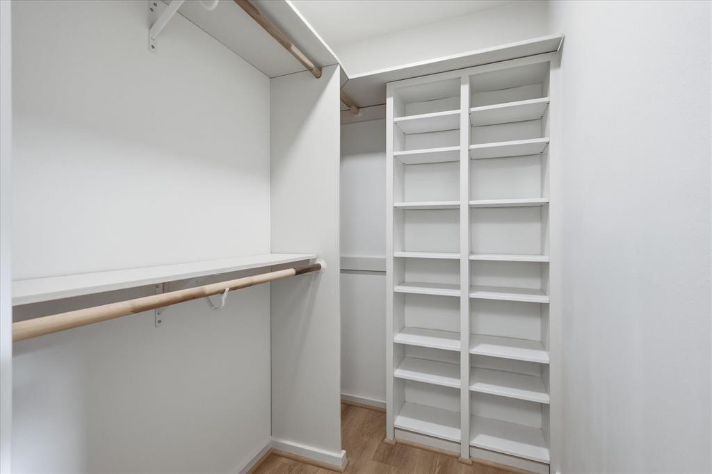 Walk-in closet featuring white built-in shelving, wooden garment rods, and wood-finish flooring