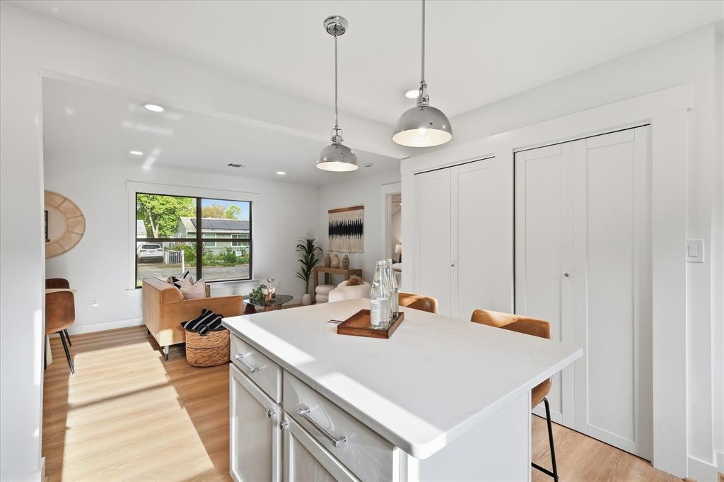 Kitchen island with a solid surface countertop, dual metal pendant lighting, wood-finish flooring, and floor-to-ceiling cabinetry