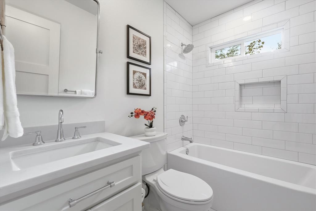 Bathroom featuring a white vanity with a composite countertop, rectangular undermount sink, white subway tile shower surround with a built-in recessed niche, and horizontal transom window