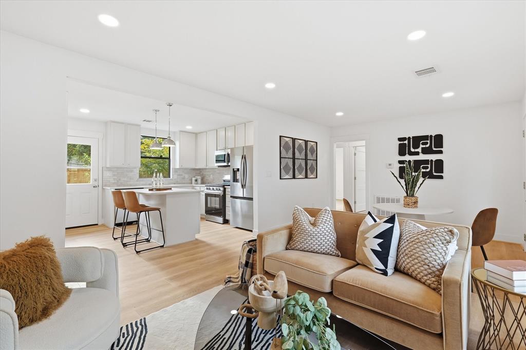 Open-concept kitchen featuring white shaker-style cabinetry, stainless steel appliances, a central island, and recessed lighting throughout with wood-finish flooring