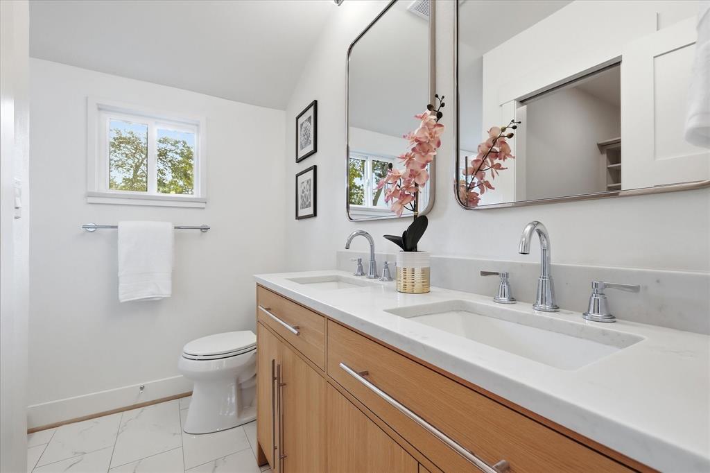 Double vanity featuring light wood cabinetry, white stone countertops, dual under-mount sinks, chrome widespread faucets, and twin rectangular mirrors