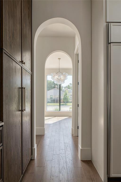 Arched architectural detail featuring floor-to-ceiling dark-stained cabinetry, wood-finish flooring, and a multi-light bubble chandelier