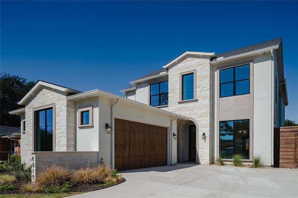Two-story exterior featuring light stone masonry, smooth stucco siding, black-framed windows, a wood-finish garage door, and a covered arched entryway