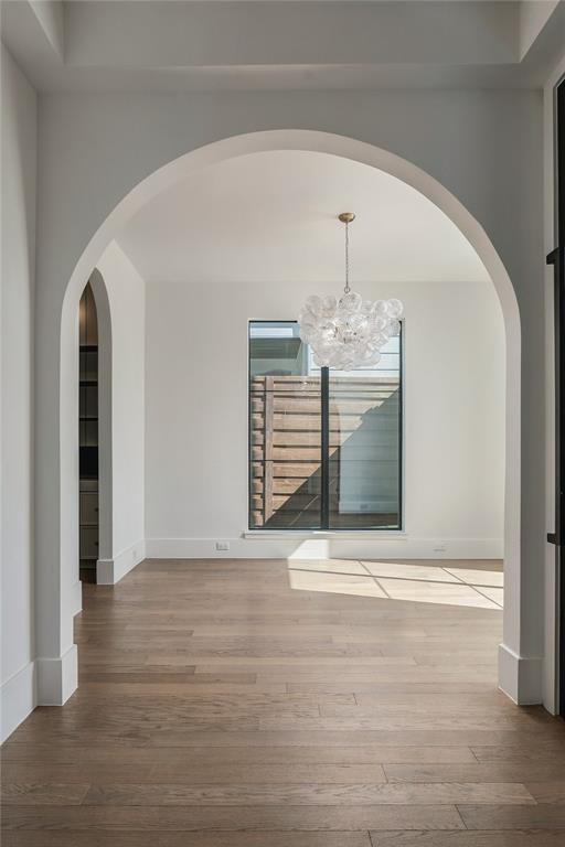 Architectural arched entryways featuring neutral wall finishes, wood-finish flooring, and a multi-globe glass pendant chandelier, complemented by a large window with black framing