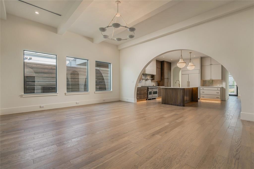 Expansive open-concept space featuring a grand architectural archway, wood-finish flooring, a modern multi-pendant chandelier, and custom kitchen cabinetry with a central island