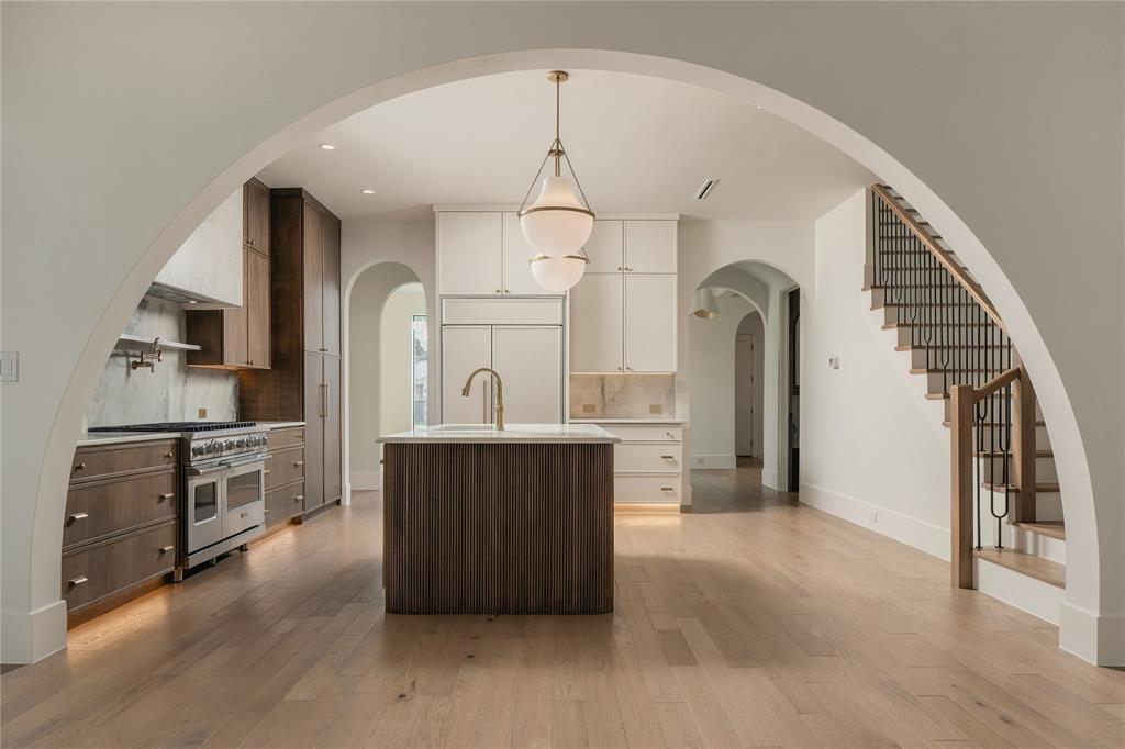 Kitchen featuring a large central island, custom dual-tone cabinetry, professional-grade range, wood-finish flooring, and a prominent arched entryway