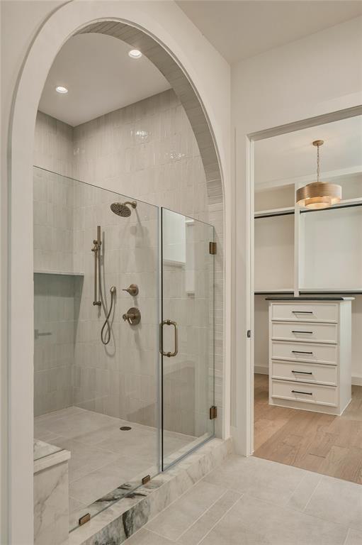 Walk-in shower featuring an arched entry, glass enclosure, stone-tiled floor, and brass-finish fixtures, complemented by a built-in chest of drawers with an integrated countertop