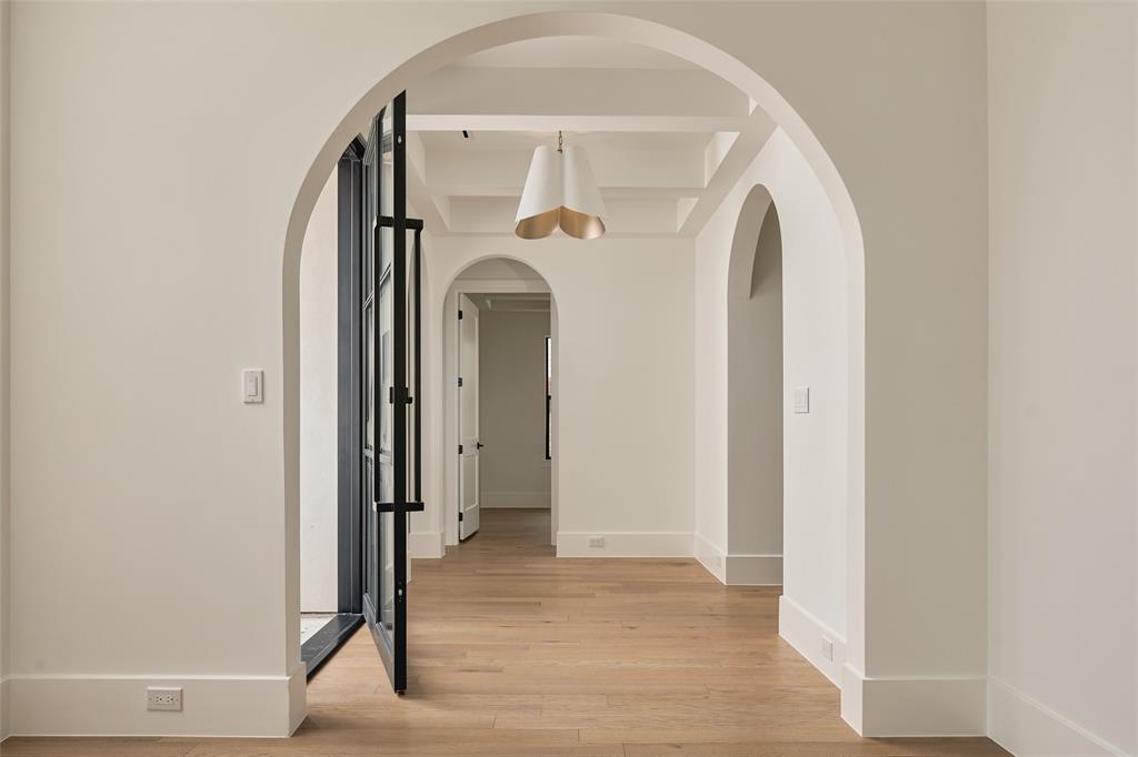 Interior featuring arched doorways, wood-finish flooring, coffered ceilings, and a decorative pendant light fixture
