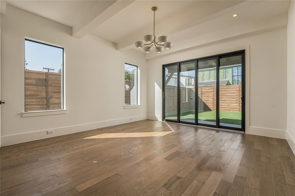 Open-concept room featuring wood-finish flooring, tray ceilings, a modern multi-bulb chandelier, and black-framed sliding glass doors opening to a fenced exterior area
