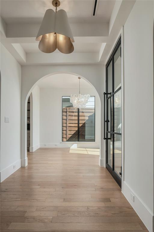 Entryway featuring wood-finish flooring, a tray ceiling, an arched passage, a black-framed glass door, and decorative pendant lighting