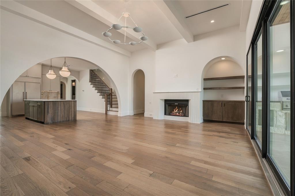 Open-concept living space featuring high ceilings with exposed beams, wood-finish flooring, a fireplace with integrated cabinetry, and multi-panel sliding glass doors