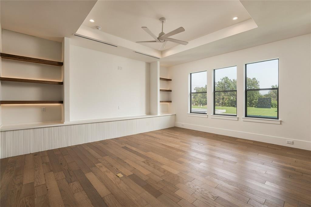 Tray ceiling with recessed lighting, wood-finish flooring, built-in shelving with integrated lighting, and three paneled windows