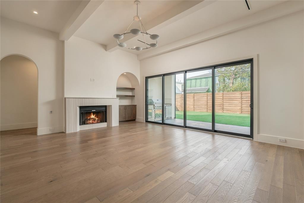 Living area featuring wood-finish flooring, vaulted ceiling with exposed beams, fireplace with fluted surround, built-in arched shelving, and oversized multi-panel sliding glass doors