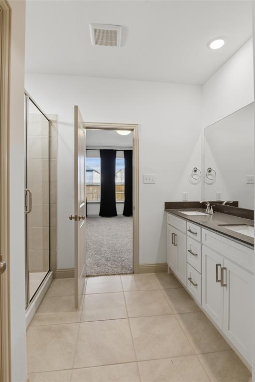 Bathroom featuring a dual-sink vanity with white cabinetry, dark solid-surface countertops, large wall-mounted mirror, and a glass-enclosed shower with tile surround