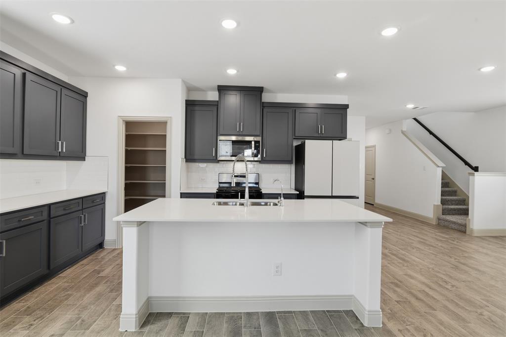 Kitchen featuring charcoal cabinetry, central island with quartz countertop, walk-in pantry, wood-finish flooring, and recessed lighting