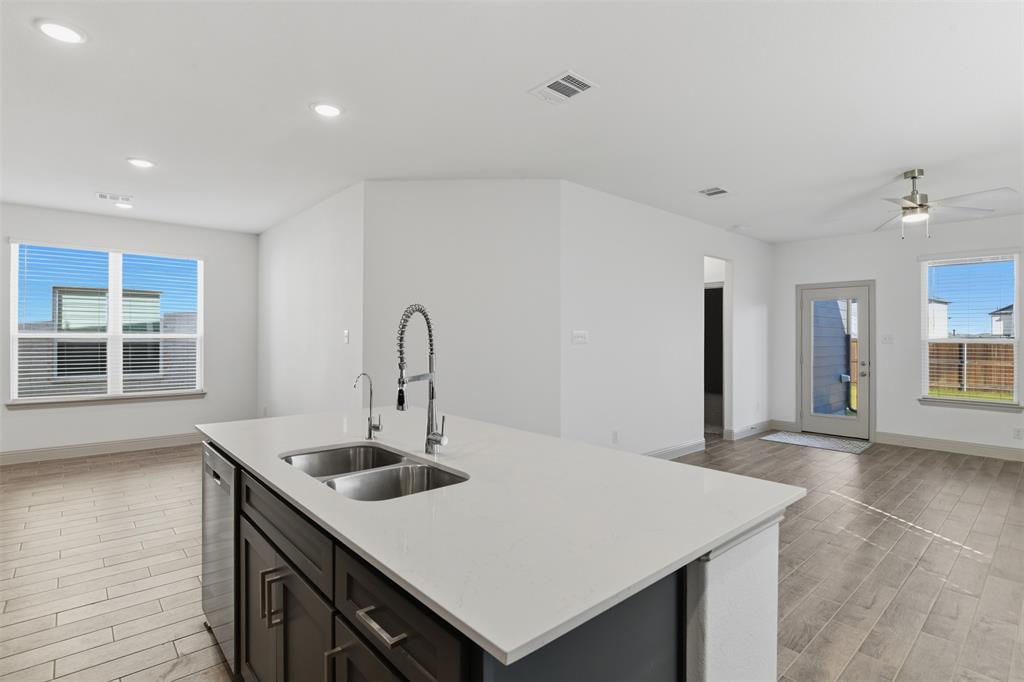 Kitchen island featuring a stone-composite countertop, dual-basin stainless steel sink, gooseneck faucet, dark-finish shaker cabinetry, and wood-finish flooring
