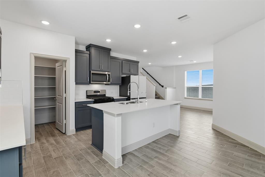 Kitchen featuring dark cabinetry, solid-surface countertops, center island with undermount sink, built-in stainless steel microwave, and wood-finish tile flooring
