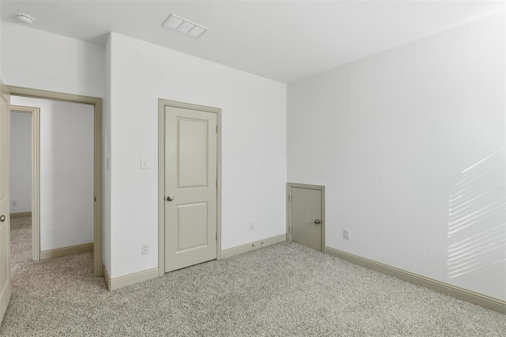 Neutral interior space featuring textured wall-to-wall carpeting, crisp white walls, neutral-toned interior doors, and a built-in under-stair storage access door