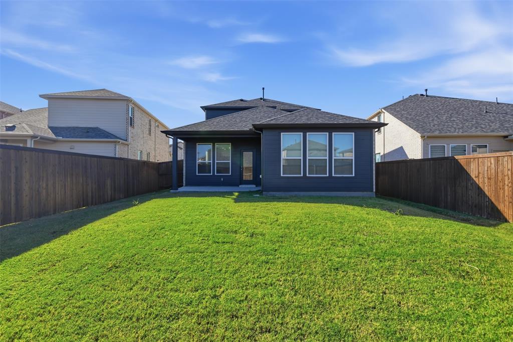 Fenced backyard featuring a manicured lawn, dark-toned exterior siding, multiple rectangular windows, and a covered rear patio
