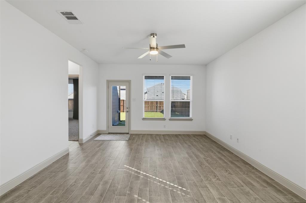 Neutral-toned interior space featuring wood-finish flooring, dual windows, a central ceiling fan with integrated lighting, and a glass-paneled exterior door