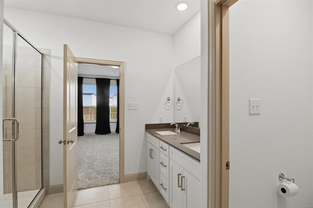 Bathroom featuring a dual-sink vanity with a solid-surface countertop, glass-enclosed shower with tile surround, and tile flooring