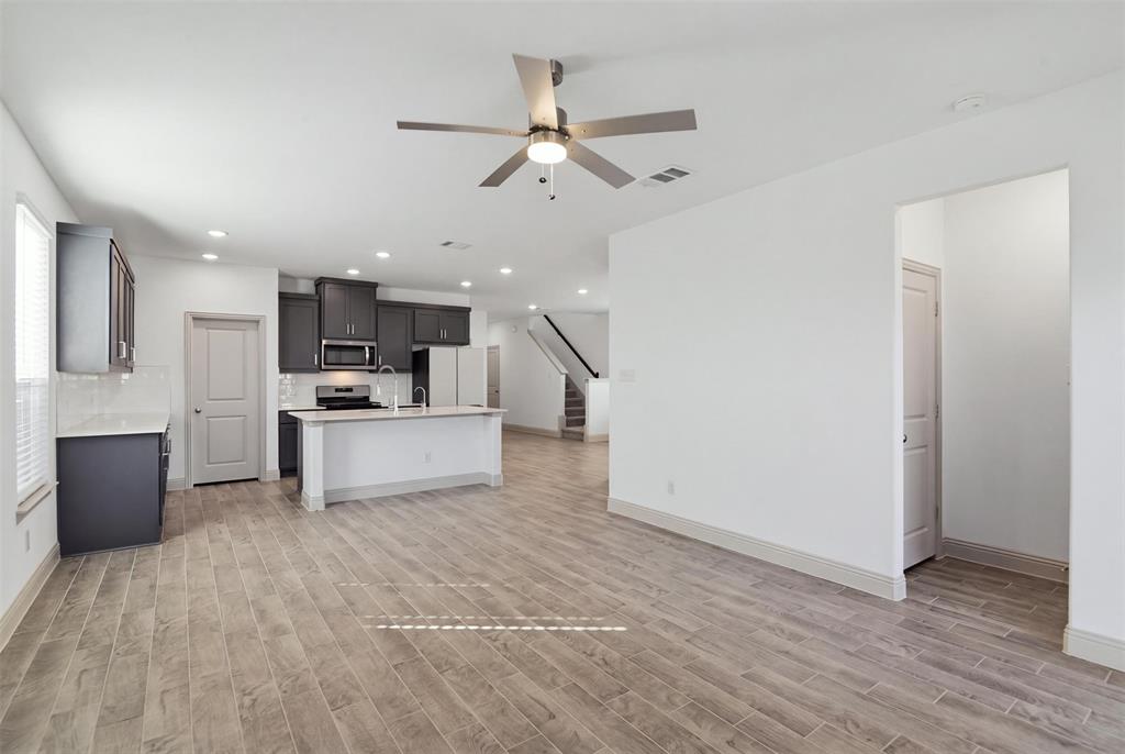 Open-concept interior featuring wood-finish tile flooring, recessed lighting, a modern ceiling fan, dark cabinetry, and a kitchen island with a stone-finish countertop