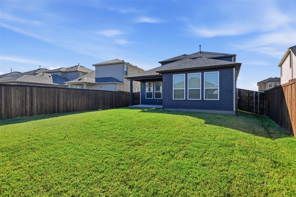 Expansive backyard featuring a sod lawn, horizontal wood-plank fencing, covered concrete patio, dark-toned siding, and energy-efficient windows