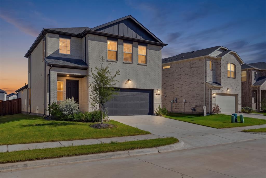 Two-story exterior featuring light-toned brick masonry, vertical metal paneling accents, and a two-car garage