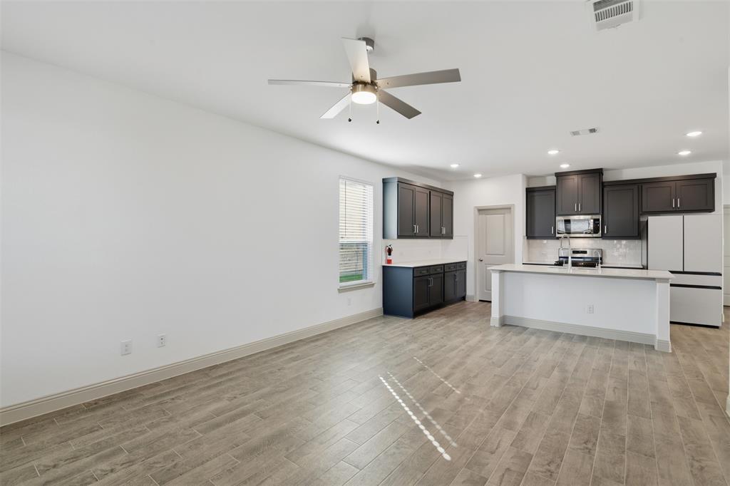 Open-concept kitchen featuring dark-finish cabinetry, a white countertop island with an integrated sink, wood-finish flooring, recessed lighting, and a modern ceiling fan