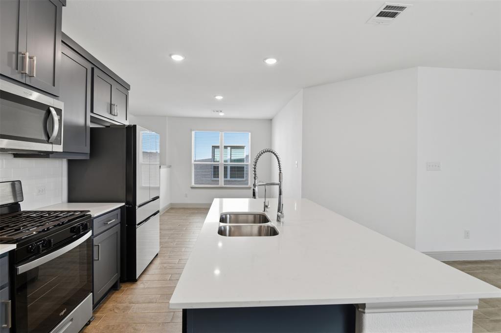 Kitchen featuring shaker-style cabinetry, quartz countertops, a dual-basin stainless steel sink with a high-arch faucet, and wood-finish flooring