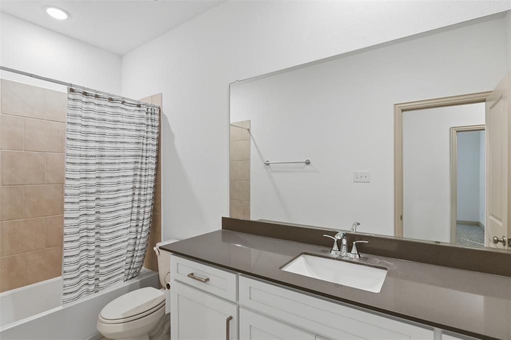 Bathroom featuring white cabinetry, quartz countertop with an integrated rectangular sink, large wall-mounted mirror, and tile-surround shower
