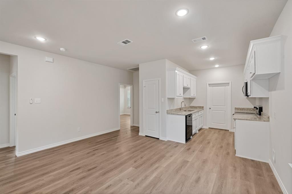Open interior space featuring wood-finish flooring, recessed lighting, white cabinetry, neutral stone-finish countertops, and a stainless steel sink