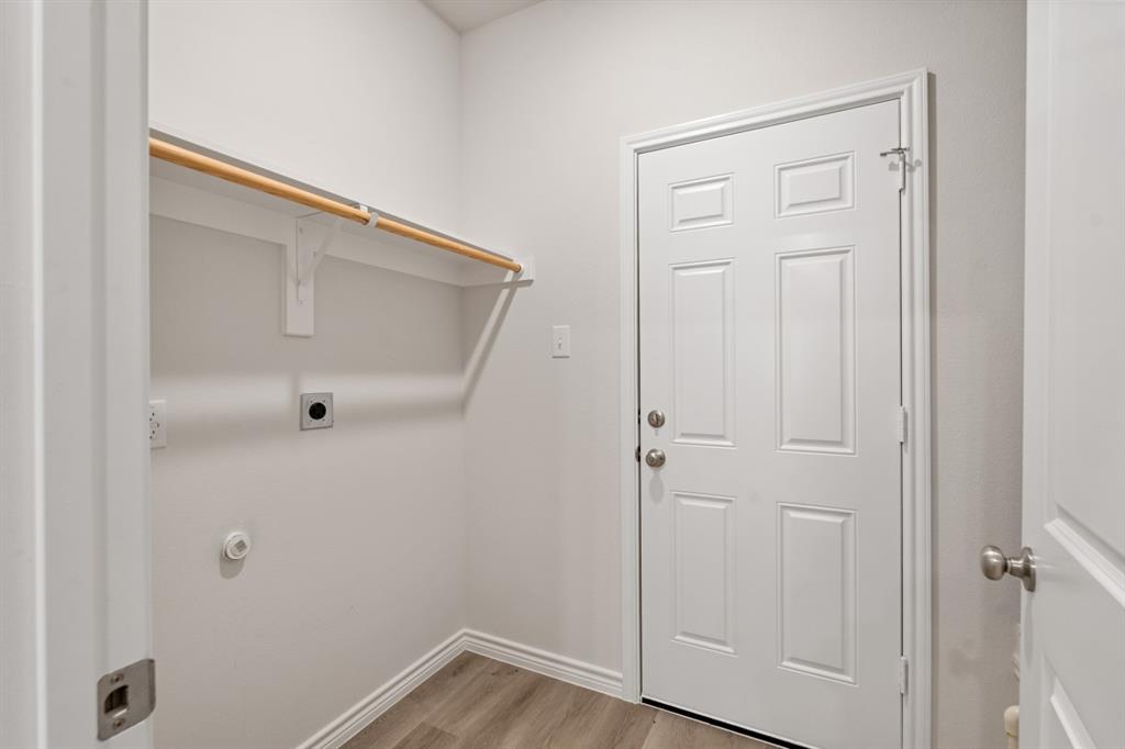 Utility room featuring wood-finish flooring, a six-panel door, and a built-in wall-mounted garment rod