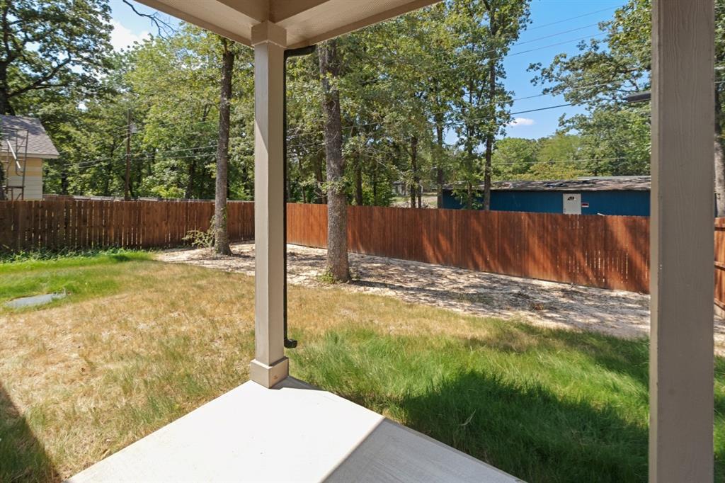 Covered porch featuring concrete flooring and wooden support columns, overlooking a fenced backyard with mature trees