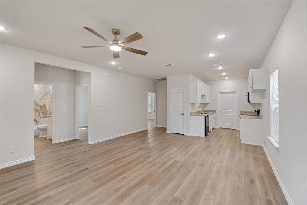 Open-concept interior featuring wood-finish flooring, recessed lighting, a ceiling fan with integrated light, and a kitchen area with white cabinetry and stone-surfaced countertops