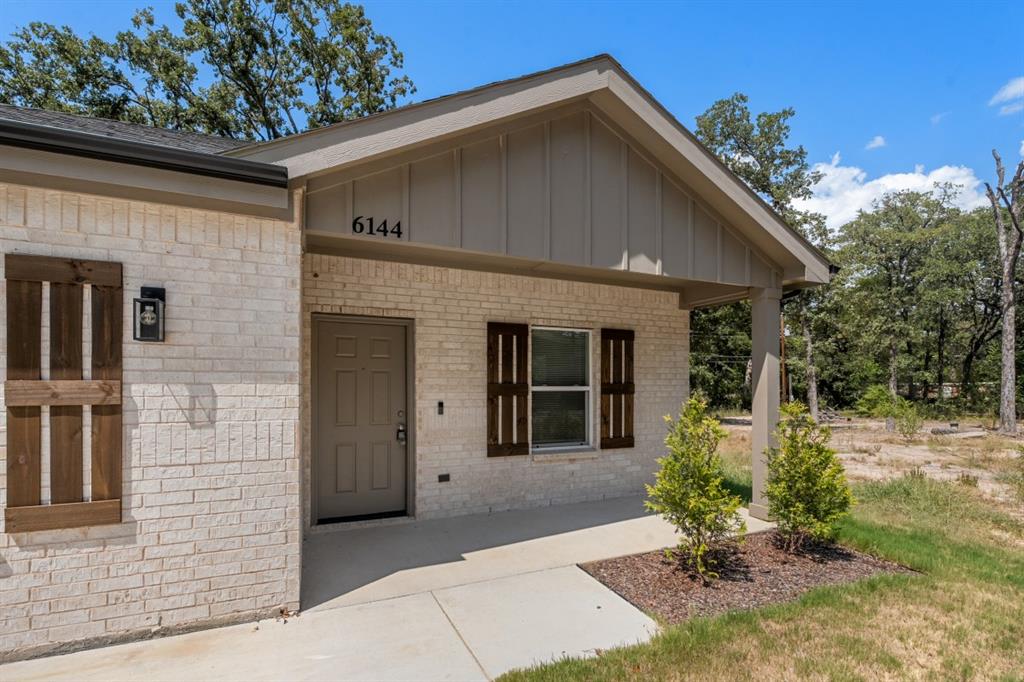 Light-colored brick exterior featuring board-and-batten siding, dark wood-tone shutters, a covered concrete porch, and rectangular wall-mounted exterior lighting