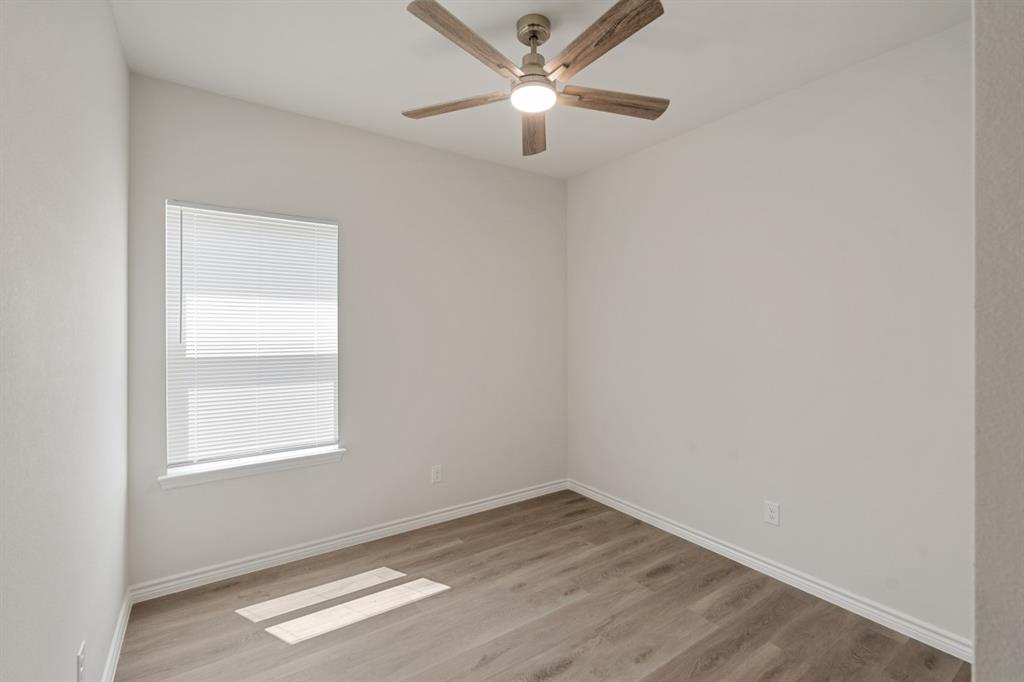 Neutral-toned interior space featuring wood-finish flooring, a ceiling fan with integrated lighting, and a single-hung window with installed blinds