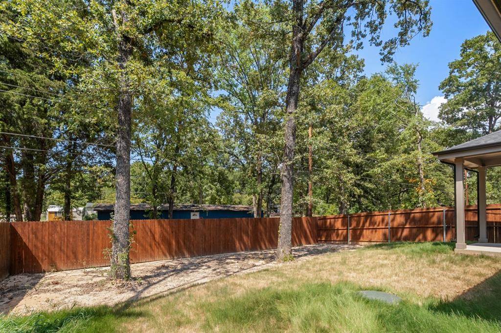 Backyard featuring a wood-panel fence, mature trees, and a covered patio area