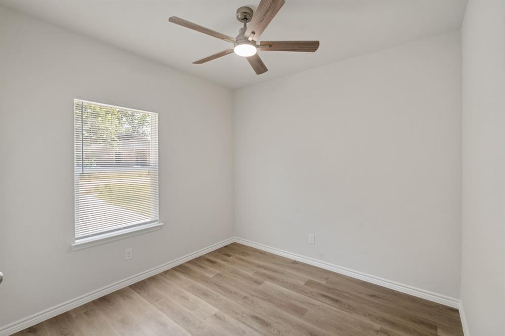 Neutral-toned interior space featuring wood-finish flooring, a ceiling fan with integrated lighting, and a single-pane window