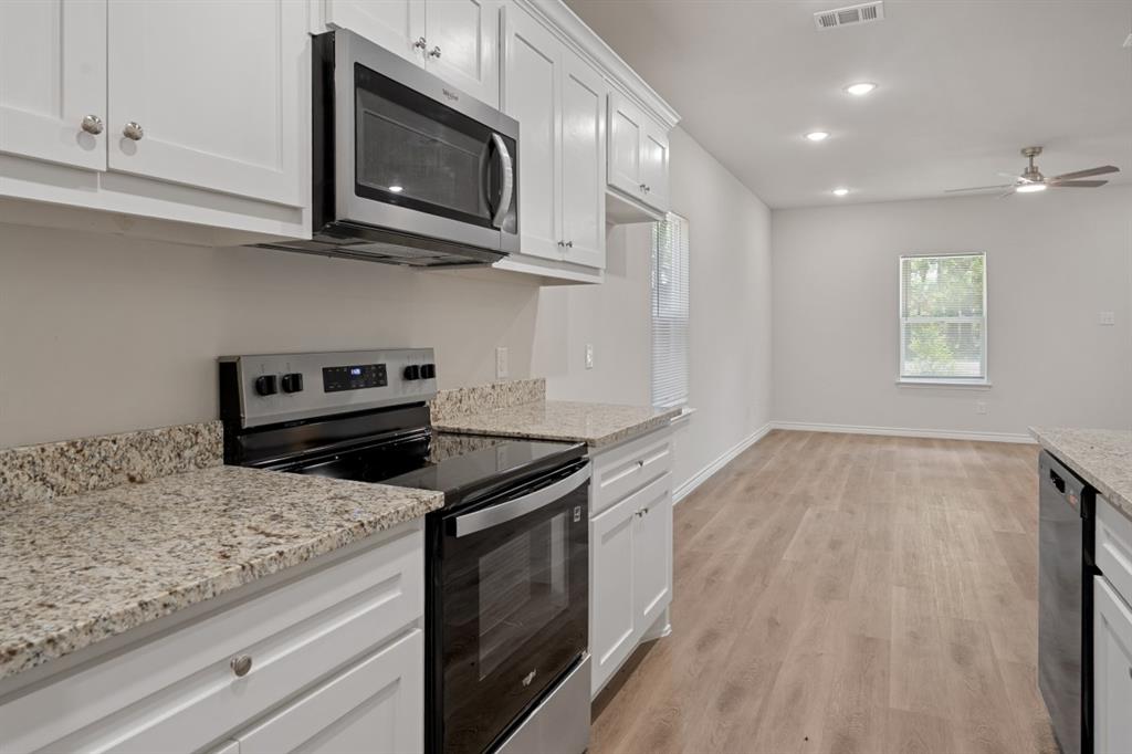 Kitchen featuring white shaker-style cabinetry, stone-finish countertops, stainless steel appliances, and wood-finish flooring
