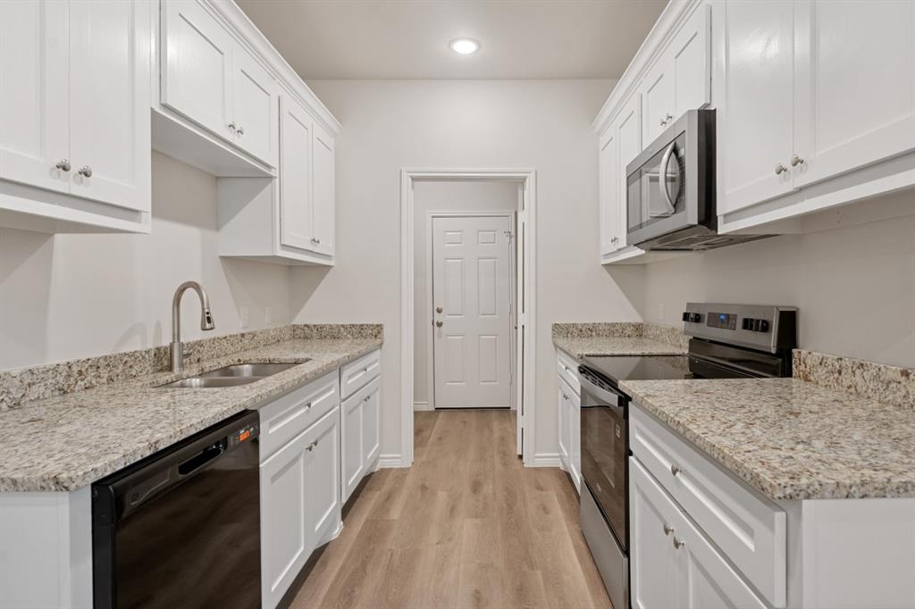 Kitchen featuring white Shaker-style cabinetry, stone-finish countertops, stainless steel appliances, and wood-finish flooring