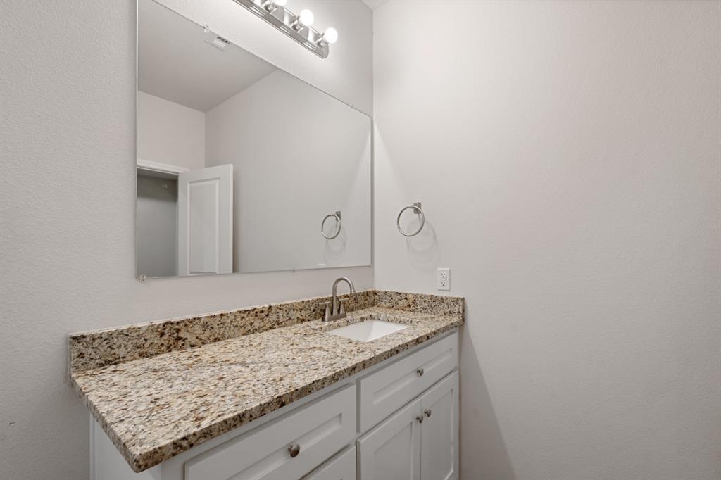 White vanity cabinetry featuring an integrated stone countertop, undermount rectangular sink, polished chrome faucet, and large wall-mounted mirror with multi-bulb light fixture