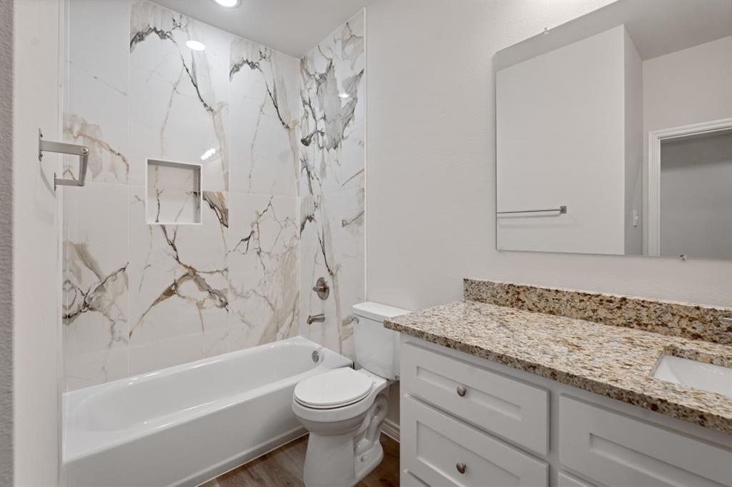 Bathroom featuring full-height stone-patterned wall tile, built-in shower niche, vanity with stone-finished countertop, undermount sink, and white cabinetry