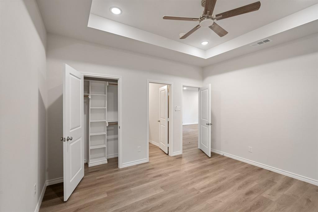 Tray ceiling with recessed lighting, wood-finish flooring, ceiling fan, and built-in closet shelving
